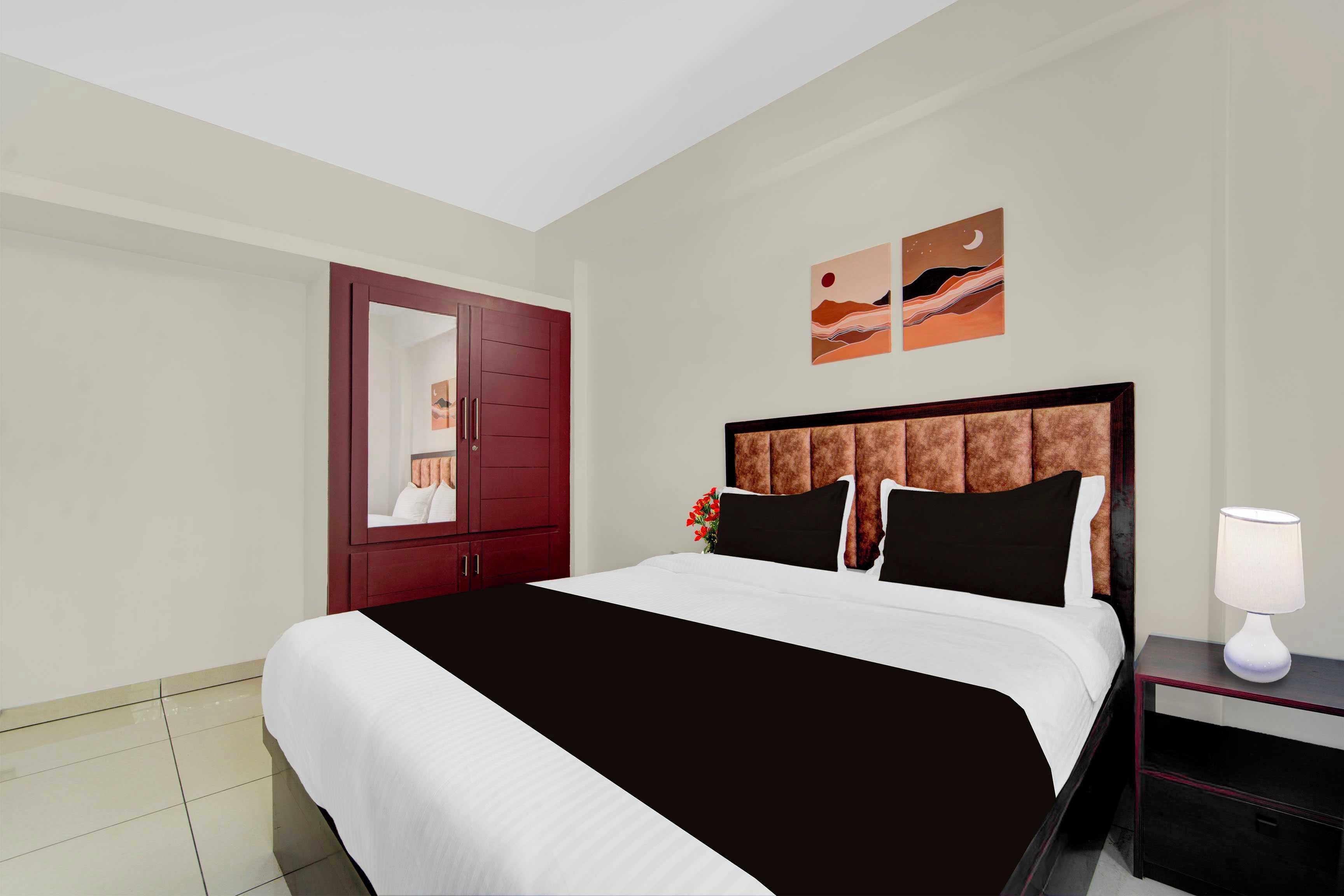 A hotel room with a large bed, a nightstand with a lamp, a wardrobe, and two wall art pieces.