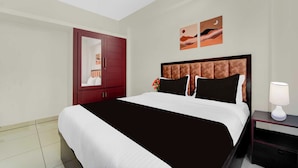 A hotel room with a large bed, a nightstand with a lamp, a wardrobe, and two wall art pieces. - Townhouse Valiyavila Bus Terminal (Trivandrum)