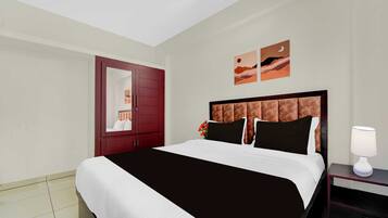 A hotel room with a large bed, a nightstand with a lamp, a wardrobe, and two wall art pieces.