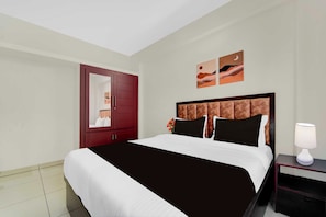 Une chambre d’hôtel avec un grand lit, une table de chevet avec une lampe, une armoire et deux œuvres d’art murales.