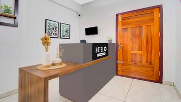 A hotel reception desk with a 'HOTEL' sign, a flat-screen TV, and framed artwork on the wall.