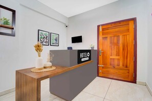 Un comptoir d'accueil d'hôtel avec une enseigne indiquant « HÔTEL », un téléviseur à écran plat et des œuvres d'art encadrées accrochées au mur.