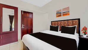 A hotel room with a large bed, a wooden wardrobe, a nightstand with a vase of flowers, and two landscape paintings on the wall. - Townhouse Valiyavila Bus Terminal (Trivandrum)