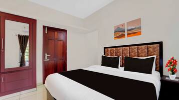 A hotel room with a large bed, a wooden wardrobe, a nightstand with a vase of flowers, and two landscape paintings on the wall.