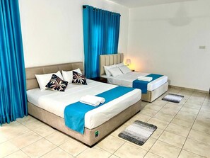 Ein Hotelzimmer mit zwei Betten, einem blauen Vorhang und einem Fliesenboden.