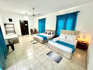Ein Hotelzimmer mit zwei Betten, einem Schreibtisch, einem Stuhl und einem Deckenventilator.