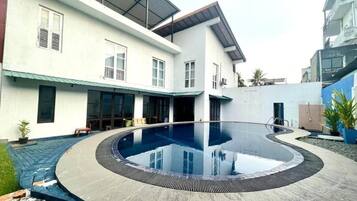 Una casa moderna con piscina circular, un porche cubierto y un ventanal grande.