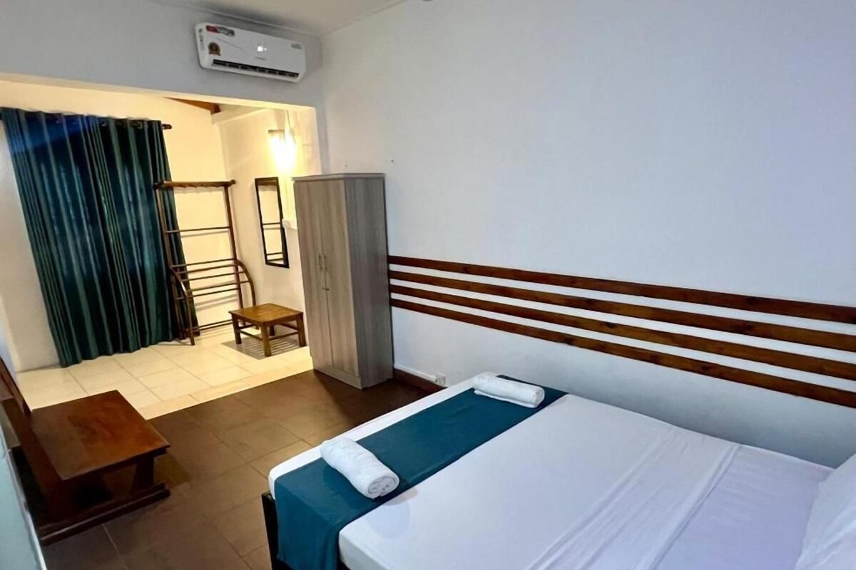 Ein Hotelzimmer mit Bett, Holz-Kopfteil, Schreibtisch, Stuhl, Kleiderschrank und einem Fenster mit Vorhängen.