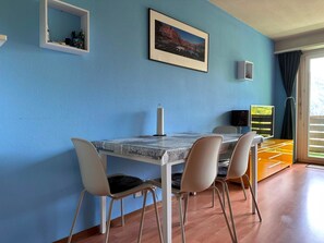 A dining area with a table and chairs, a framed picture on the wall, and a window with curtains. - Residenz Belair Leukerbad # 4-bed apartment, Bad, WC by Interhome (Leukerbad)