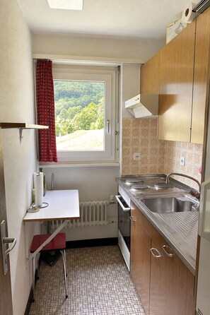 A compact kitchen with a window, a radiator, a sink, and wooden cabinets. - Residenz Belair Leukerbad # 4-bed apartment, Bad, WC by Interhome (Leukerbad)