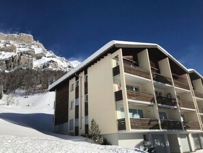 Ein mehrstöckiges Hotel mit Balkonen vor einer verschneiten Bergkulisse.