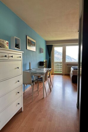 Ett rum med ett matbord, stolar, en vit byrå och utsikt över ett bergigt landskap genom ett stort fönster.