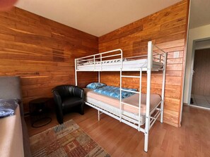 Ett rum med en våningssäng, väggar klädda med träpanel, en svart läderfåtölj och en mönstrad matta.