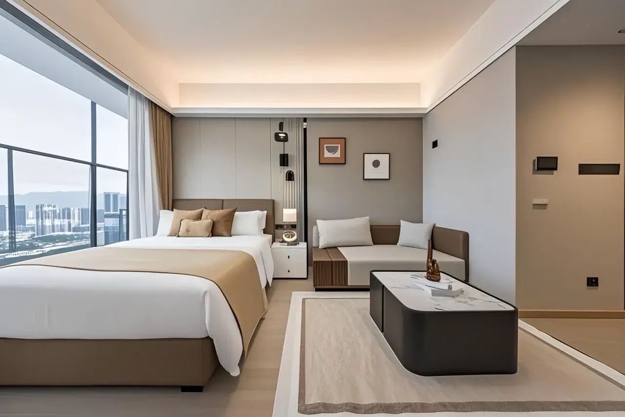 A modern hotel room with a large bed, a smaller sofa, a nightstand, and a view of the city.