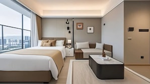 Une chambre d’hôtel moderne avec un grand lit, un petit canapé, une table de chevet et une vue sur la ville.