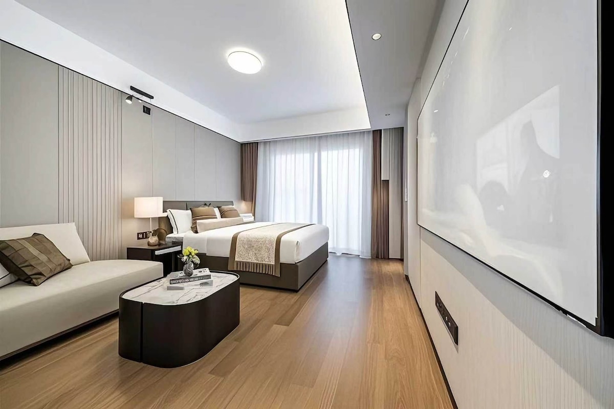 Una habitación de hotel moderna con cama, sofá, mesa de centro y una pantalla grande.