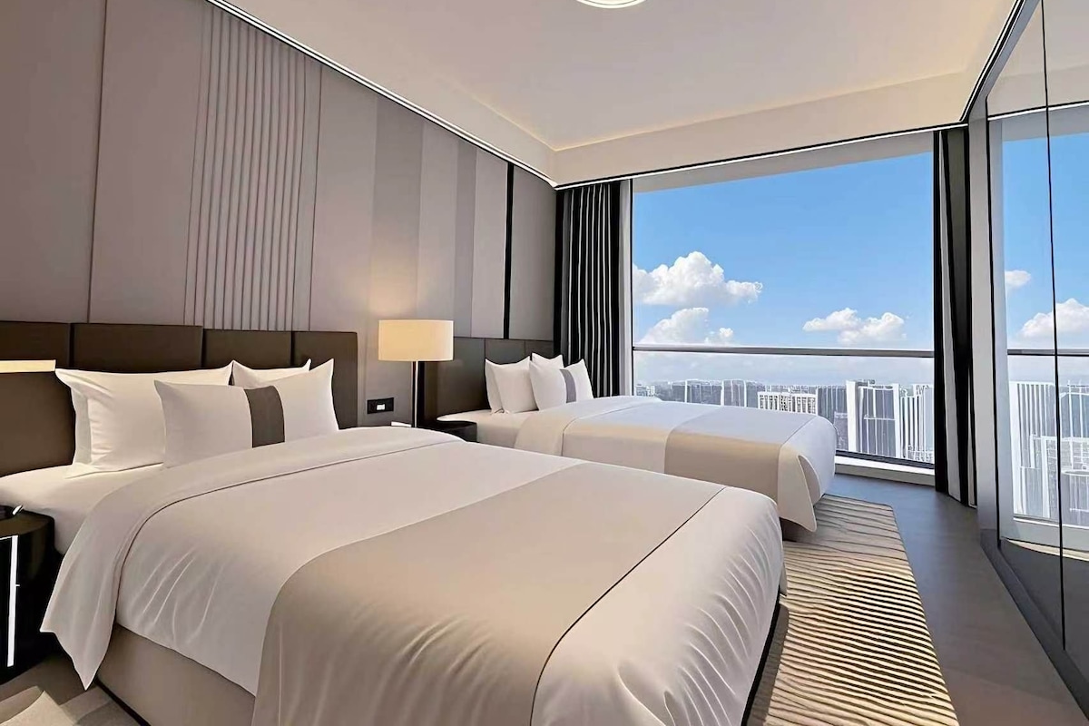 Una habitación de hotel moderna con dos camas, un ventanal amplio con vista a la ciudad y una lámpara en el techo.