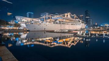 A large cruise ship docked at a port with a city skyline in the background.