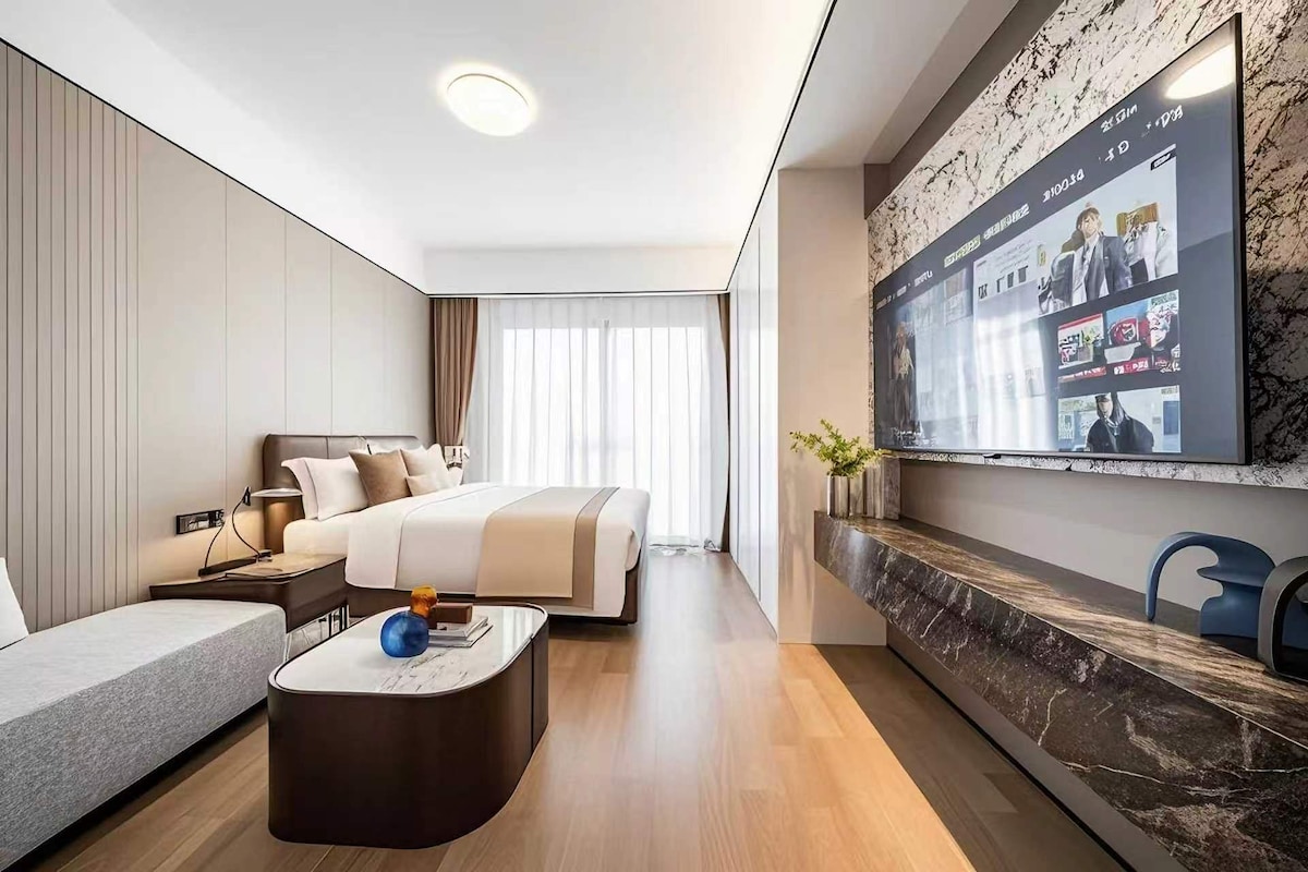 Una habitación de hotel moderna con una cama, un sofá, un televisor montado en la pared y una chimenea de mármol.