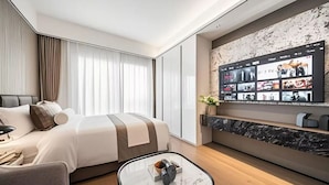 Une chambre d’hôtel moderne dotée d’un grand lit, d’un téléviseur à écran plat fixé au mur, d’une console en marbre et d’un coin salon avec une petite table.