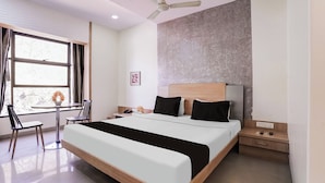 Une chambre d’hôtel avec un lit, un bureau et une chaise, un ventilateur de plafond et une fenêtre avec des rideaux.