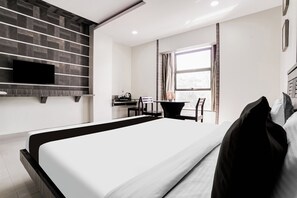 A modern hotel room with a large bed, a flat-screen TV mounted on the wall, a small desk with a chair, and a window with curtains. - Townhouse Kranti Square Aurangabad (Chhatrapati Sambhajinagar)
