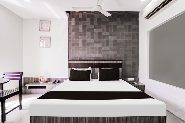 A modern hotel room with a large bed, a desk, a chair, and a ceiling fan.