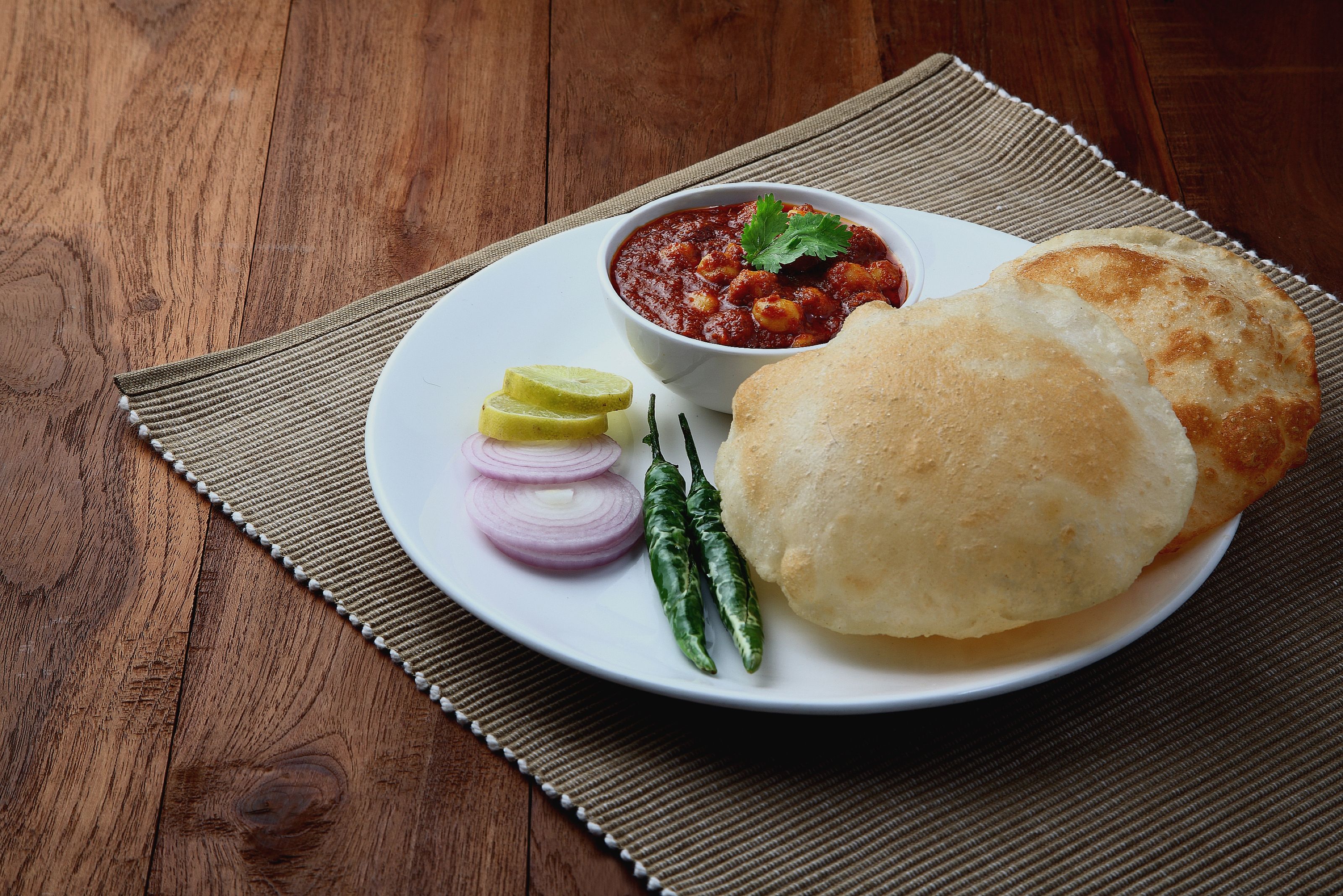 A plate with a bread roll, a bowl of sauce, slices of onion, a lime wedge, and chili peppers.