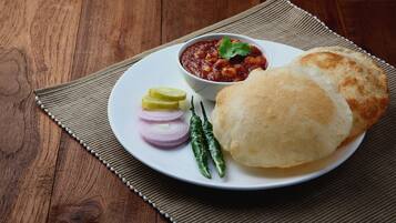 A plate with a bread roll, a bowl of sauce, slices of onion, a lime wedge, and chili peppers.