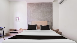 Une chambre d’hôtel moderne avec un grand lit, une table de chevet en bois, une petite table, une chaise et un climatiseur fixé au mur.