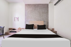 A modern hotel room with a large bed, a wooden nightstand, a small table, a chair, and a wall-mounted air conditioner. - Townhouse Kranti Square Aurangabad (Aurangabad)