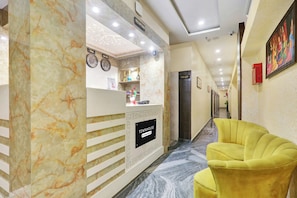 Zona de recepción de un hotel con un mostrador de mármol, un reloj y un cartel de recepción.