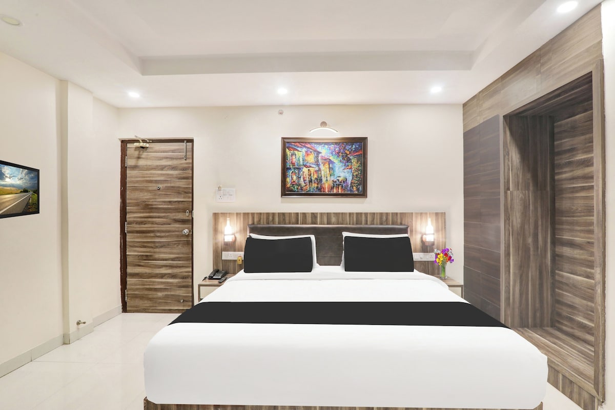 Una habitación de hotel moderna con una cama grande, una puerta de madera, un cuadro en la pared y una mesita de noche con una lámpara.