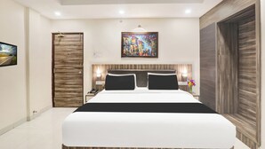 A modern hotel room with a large bed, a wooden door, a painting on the wall, and a nightstand with a lamp.