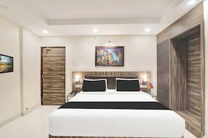 Una habitación de hotel moderna con una cama grande, una puerta de madera, un cuadro en la pared y una mesita de noche con una lámpara.