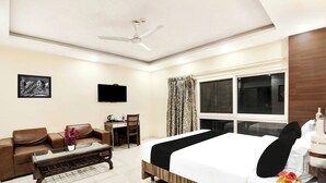 A hotel room with a bed, a desk, a chair, a sofa, a ceiling fan, and a window with curtains.
