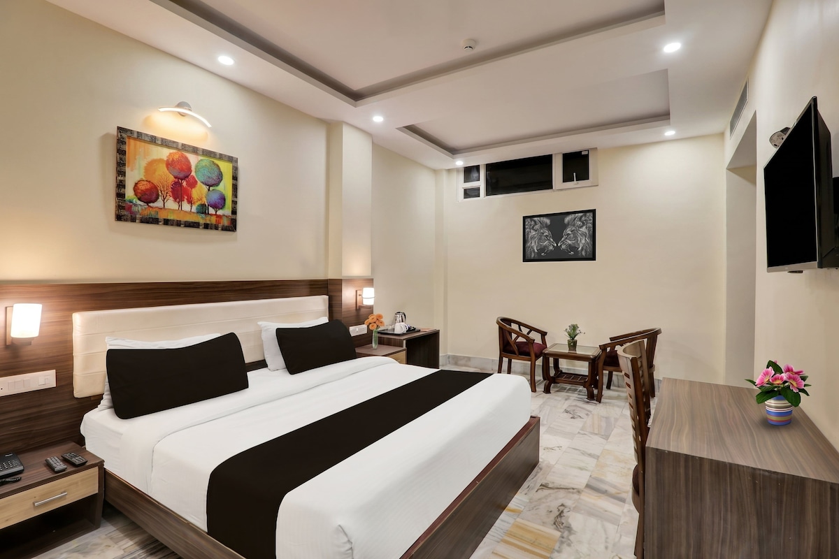 Una habitación de hotel con cama, mesita de noche, escritorio, sillas y televisión.