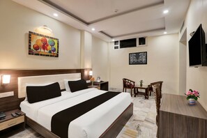 A hotel room with a bed, bedside table, nightstand, desk, chairs, and a TV.