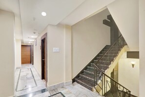 A hallway with a marble floor, a wooden door, a light switch, and a staircase with metal railings.