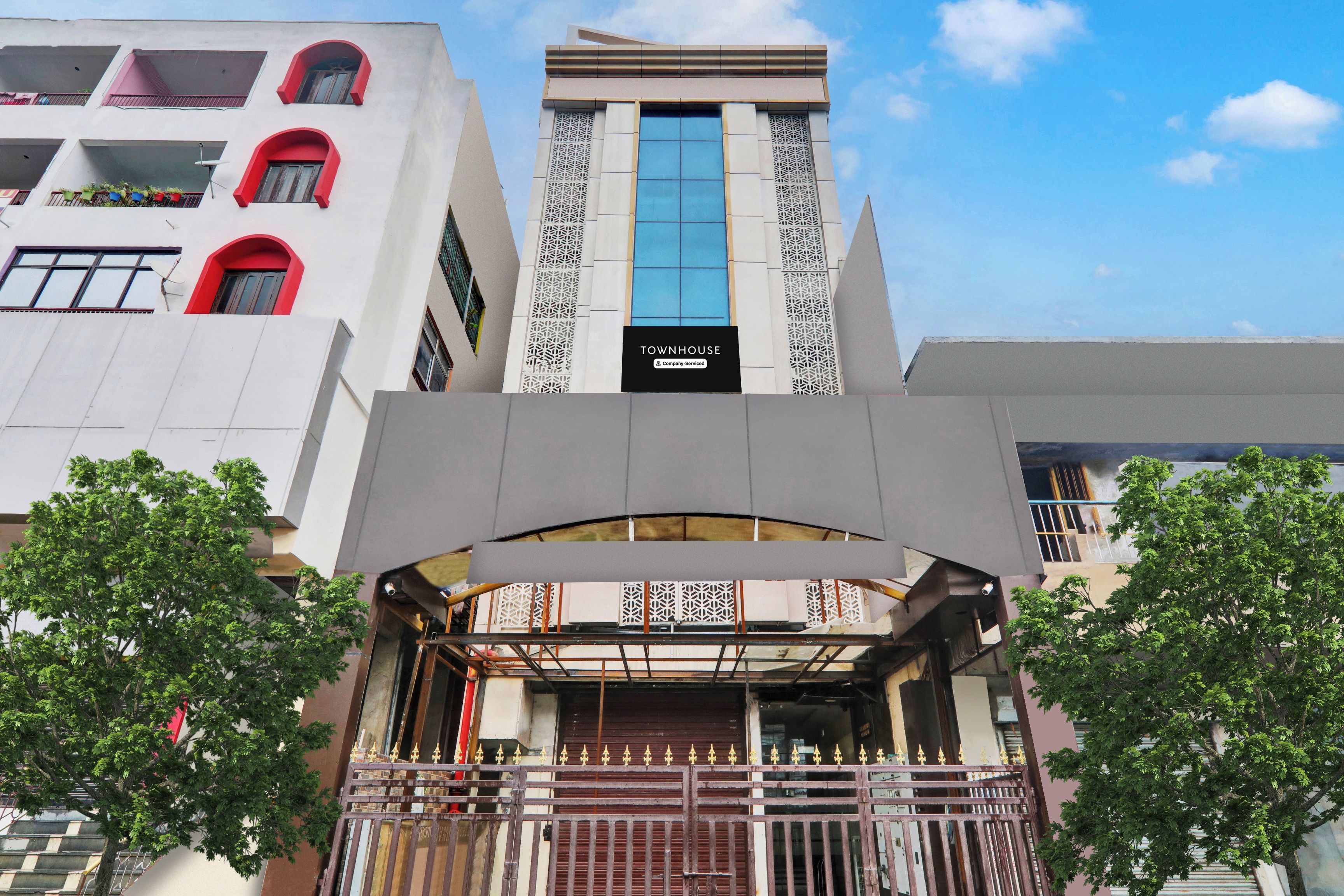 Un edificio moderno con un llamativo letrero 'TOWNHOUSE', una entrada central con un arco decorativo y una entrada protegida por una reja.
