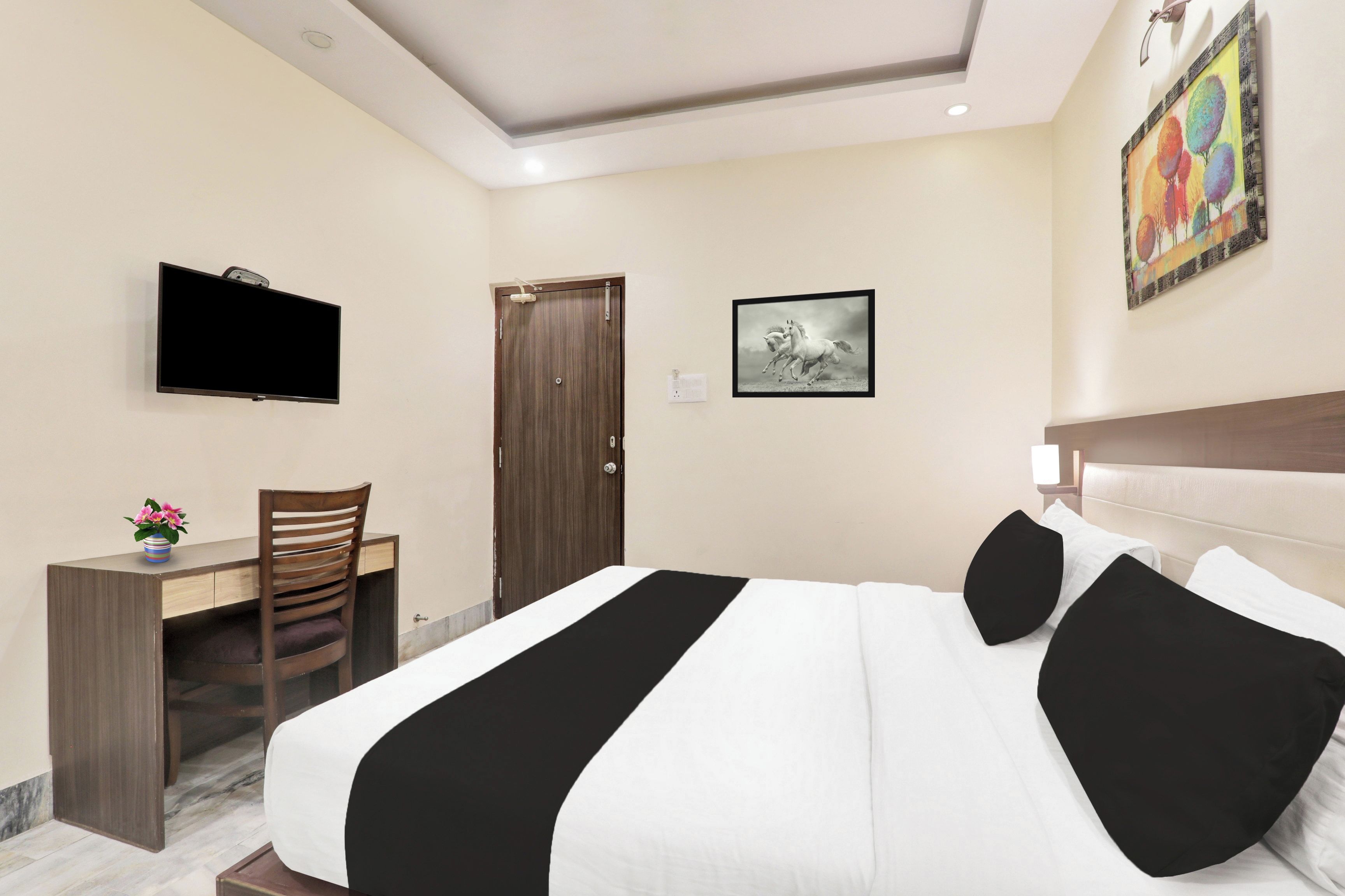 A hotel room with a bed, a desk, a chair, a TV, and a door.