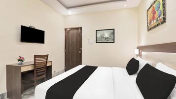 A hotel room with a bed, a desk, a chair, a TV, and a door.