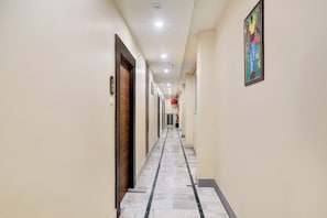 En hotellkorridor med dörrar på båda sidor, ett kaklat golv och en tavla på väggen till höger.