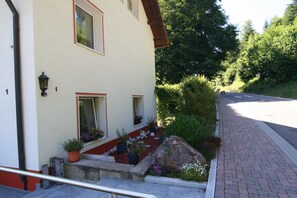 A building with a white facade, multiple windows, and a small garden with potted plants and flowers. - Haus Monika (Todtmoos)