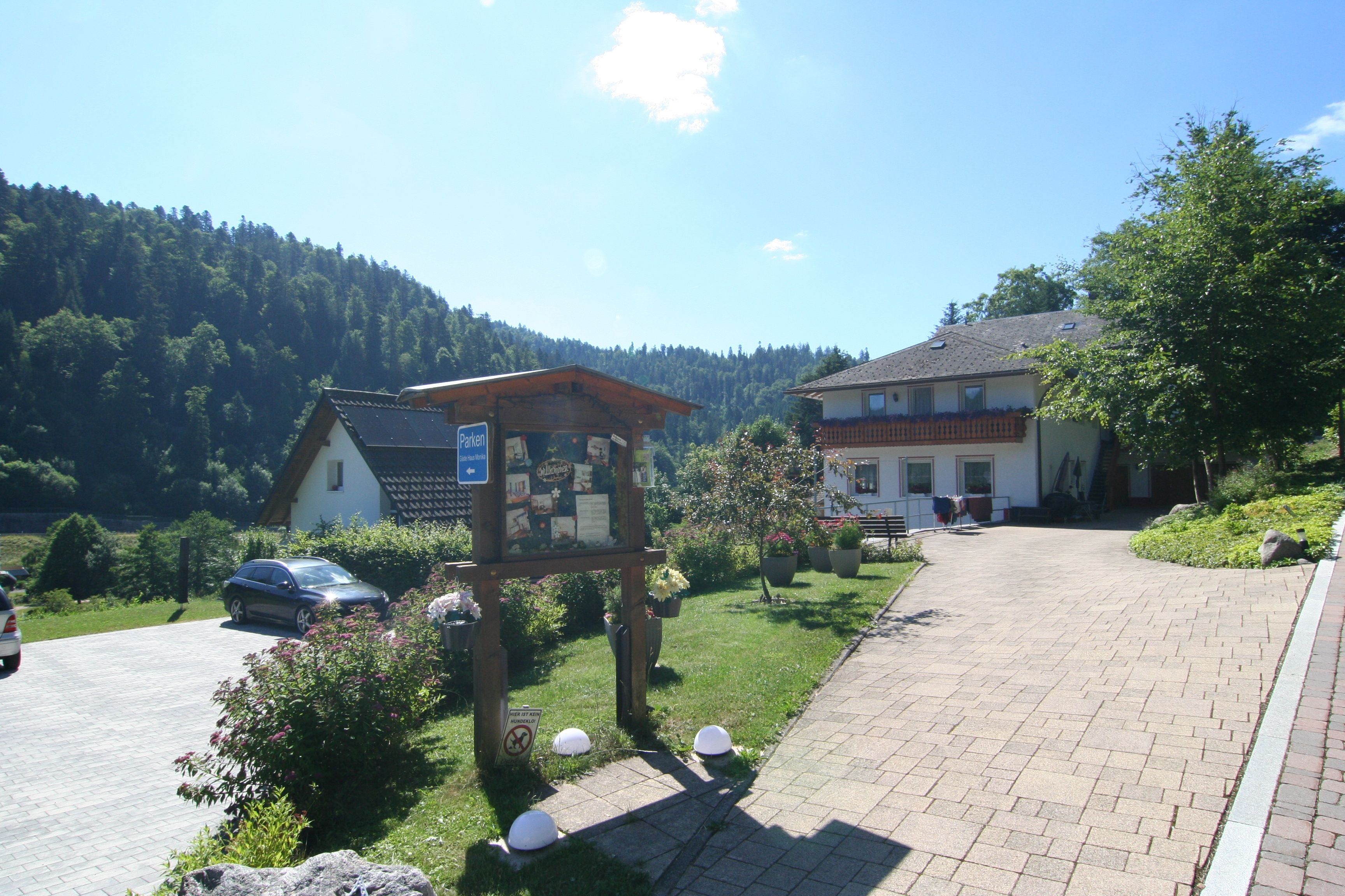 Un paysage rural avec un panneau indicateur en bois, une allée pavée et un bâtiment doté d’un toit en pente.