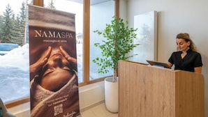A reception area with a wooden desk, a potted plant, and a poster advertising massages and care services. - Belambra Club Les Saisies - Les Embrunes - Winter & Summer (Villard-sur-Doron)