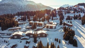 Een bergresort bedekt met sneeuw, met meerdere gebouwen, skipistes en dichte bossen.