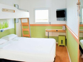 Una habitación de hotel con literas, un escritorio con silla, un televisor y una ventana.