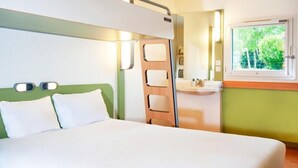 A room with a bed, a window with a view of greenery, a bedside table, and a mirror. - Ibis Budget Flers Grands Champs (Flers)
