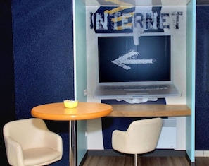 Una habitación con una pantalla grande que muestra 'INTERNET' y una flecha apuntando a la izquierda, una mesita redonda con un bol y dos sillas.